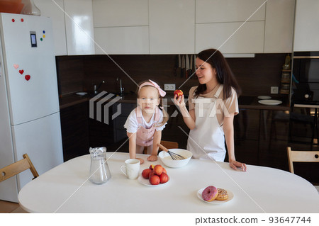 happy baby girl eating fruit and drinking water sitting at the table in the kitchen. 93647744
