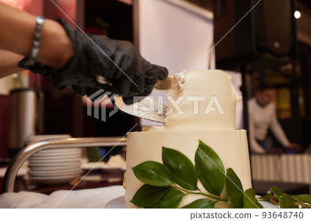 The bride and groom at the banquet together cut the wedding cake, holding on to one knife. Wedding details close-up. 93648740