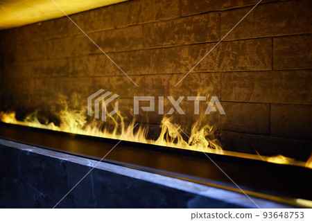 Side view on electric fireplace with artificial sparkling flame, decor for the interior, blue and orange flame with suspended swing chair in reflection. 93648753
