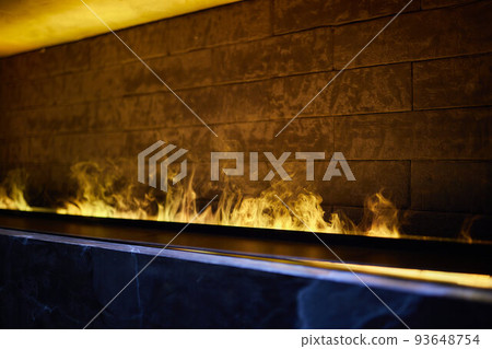 Side view on electric fireplace with artificial sparkling flame, decor for the interior, blue and orange flame with suspended swing chair in reflection. Side view on electric fireplace with artificial sparkling flame, decor for the interior, blue and orange flame with suspended swing chair in reflection. 93648754