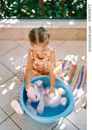 Little girl washes with soap in a bowl on the balcony of a plush hare. High quality photo Little girl washes with soap in a bowl on the balcony of a plush hare. High quality photo 93649873