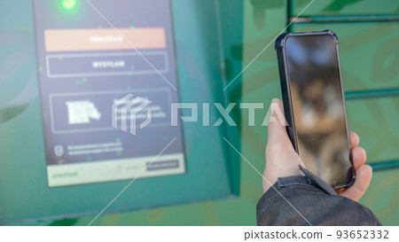 Female hand holding mobile phone next to Parcel locker Collecting parcel from shopping locker. Woman Skans QR Code on Mobile phone Self-service Locker Cell with Bar code Reader Modern Shipping and Female hand holding mobile phone next to Parcel locker Collecting parcel from shopping locker. Woman Skans QR Code on Mobile phone Self-service Locker Cell with Bar code Reader Modern Shipping and 93652332