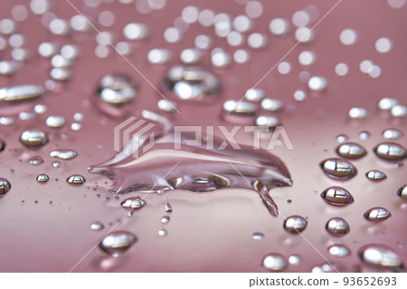 A large drop and splashes of micellar water on a pink background. A large drop and splashes of micellar water on a pink background. 93652693
