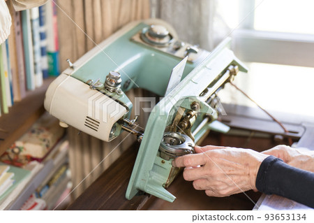 Senior woman attaching bobbin to sewing machine 93653134