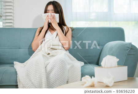 Ill Asian young woman cold covered with blanket sitting on sofa 93656220