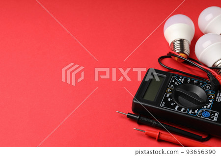 Multimeter and energy saving bulbs on red background Multimeter and energy saving bulbs on red background 93656390
