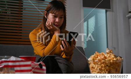 Young woman in warm sweater using mobile phone on couch, spending time in cozy winter or autumn weekend at night Young woman in warm sweater using mobile phone on couch, spending time in cozy winter or autumn weekend at night 93656957