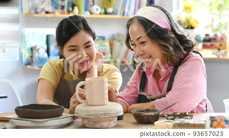 Happy retired woman and young woman creating handmade ceramic bowl in craft workshop Happy retired woman and young woman creating handmade ceramic bowl in craft workshop 93657023