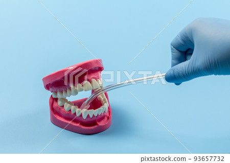 Dentist's hand in glove with saliva ejector and human jaw layout. 93657732