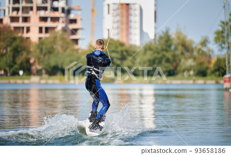 Back view of wakeboarder surfing on lake. Young surfer having fun wakeboarding in the cable park. Water sport, outdoor activity concept. 93658186