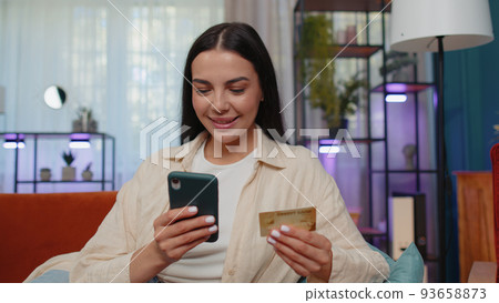 Lovely girl using credit bank card and smartphone, transferring money, purchases online shopping Lovely girl using credit bank card and smartphone, transferring money, purchases online shopping 93658873