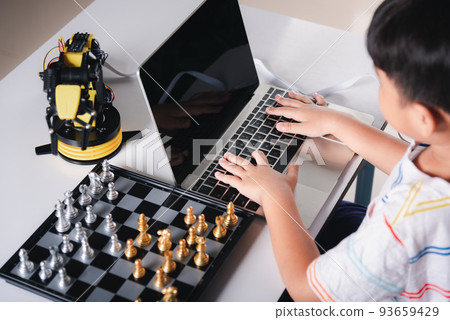 Asian little boy programming code to robot machine arm on laptop for play chess Asian little boy programming code to robot machine arm on laptop for play chess 93659429