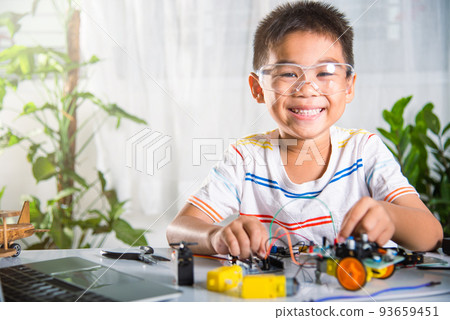Asian kid boy plugging energy and signal cable to sensor chip with Arduino robot car 93659451