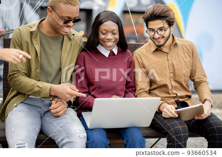Multiracial students watch some on laptop outdoors Multiracial students watch some on laptop outdoors 93660534