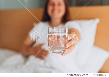Pregnant woman with glass of water sitting on bed at home. Millennial Caucasian woman wake up in cozy white bed in modern apartment in the morning. Concept of healthy lifestyle, selective focus Pregnant woman with glass of water sitting on bed at home. Millennial Caucasian woman wake up in cozy white bed in modern apartment in the morning. Concept of healthy lifestyle, selective focus 93660807