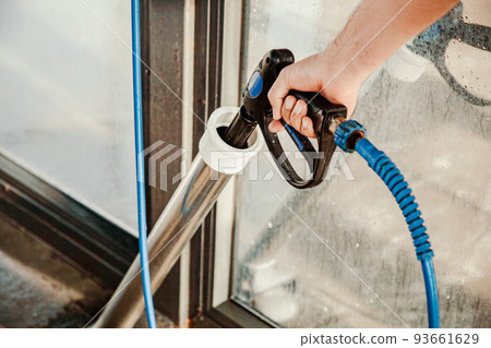 A man takes a pistol with a hose with pressurized water to wash his car at a self-service car wash A man takes a pistol with a hose with pressurized water to wash his car at a self-service car wash 93661629