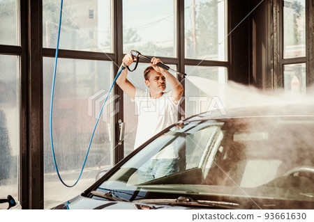 A man washes his car at a self-service car wash using a hose with pressurized water A man washes his car at a self-service car wash using a hose with pressurized water 93661630