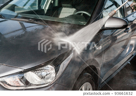 A man washes his car at a self-service car wash using a hose with pressurized water A man washes his car at a self-service car wash using a hose with pressurized water 93661632
