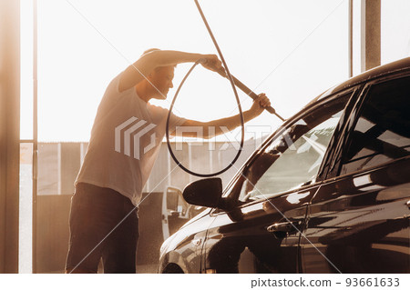 A man washes his car at a self-service car wash using a hose with pressurized water A man washes his car at a self-service car wash using a hose with pressurized water 93661633