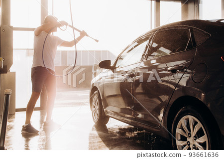 A man washes his car at a self-service car wash using a hose with pressurized water A man washes his car at a self-service car wash using a hose with pressurized water 93661636