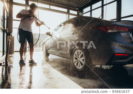 A man washes his car at a self-service car wash using a hose with pressurized water A man washes his car at a self-service car wash using a hose with pressurized water 93661637