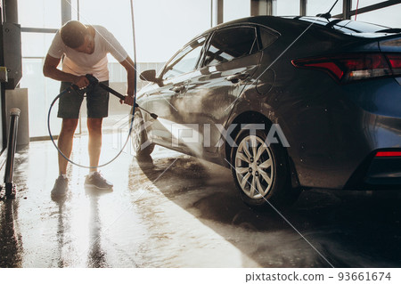 A man washes his car at a self-service car wash using a hose with pressurized water A man washes his car at a self-service car wash using a hose with pressurized water 93661674