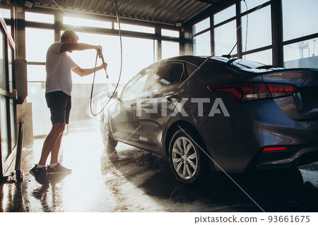 A man washes his car at a self-service car wash using a hose with pressurized water A man washes his car at a self-service car wash using a hose with pressurized water 93661675