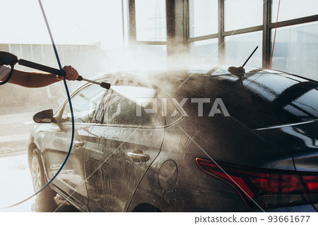 A man washes his car at a self-service car wash using a hose with pressurized water A man washes his car at a self-service car wash using a hose with pressurized water 93661677