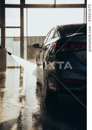 A man washes his car at a self-service car wash using a hose with pressurized water A man washes his car at a self-service car wash using a hose with pressurized water 93661679