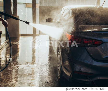 A man washes his car at a self-service car wash using a hose with pressurized water A man washes his car at a self-service car wash using a hose with pressurized water 93661680