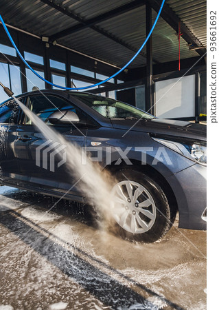 A man washes the wheels on his car at a self-service car wash using a hose with pressurized water A man washes the wheels on his car at a self-service car wash using a hose with pressurized water 93661692