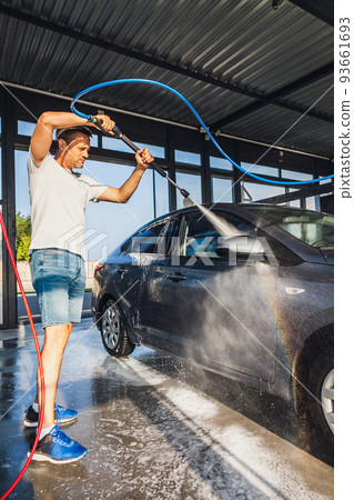 A man washes his car at a self-service car wash using a hose with pressurized water A man washes his car at a self-service car wash using a hose with pressurized water 93661693