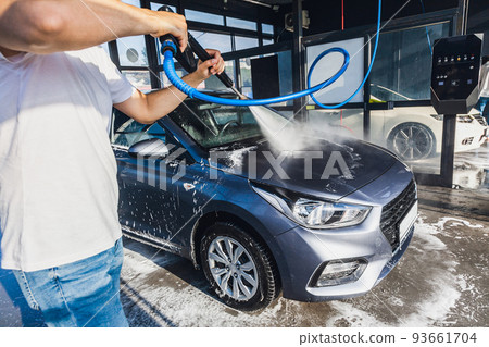 A man washes his car at a self-service car wash using a hose with pressurized water A man washes his car at a self-service car wash using a hose with pressurized water 93661704