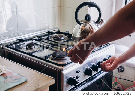 A man's hand with a match lights a gas burner or a gas stove in the kitchen A man's hand with a match lights a gas burner or a gas stove in the kitchen 93661725