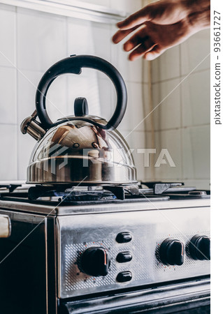The man removes the kettle from the gas burner The man removes the kettle from the gas burner 93661727