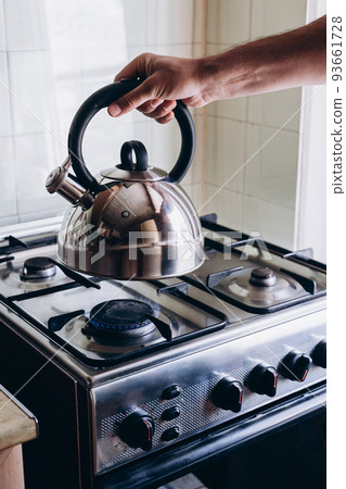 Man's hand puts the kettle on the gas burner Man's hand puts the kettle on the gas burner 93661728