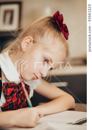 A little girl in a school uniform is doing homework in a exercise book at home A little girl in a school uniform is doing homework in a exercise book at home 93661829