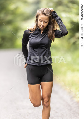 Sporty young woman stretches her leg holding feet behind her by a hand Sporty young woman stretches her leg holding feet behind her by a hand 93662862