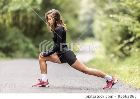 Young female athlete performs warm-up and legs stretching on a road in the nature 93662863