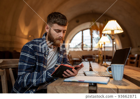 Casual business man or freelancer planning his work on notebook, working on laptop computer with smart phone, cup of coffee on table at coffee shop or home office. Casual business man or freelancer planning his work on notebook, working on laptop computer with smart phone, cup of coffee on table at coffee shop or home office. 93662871