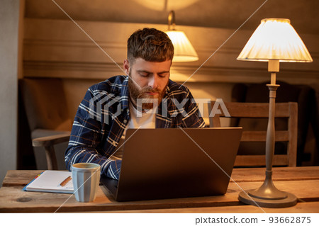 Young professional surfing the Internet on his laptop in a cafe Young professional surfing the Internet on his laptop in a cafe 93662875