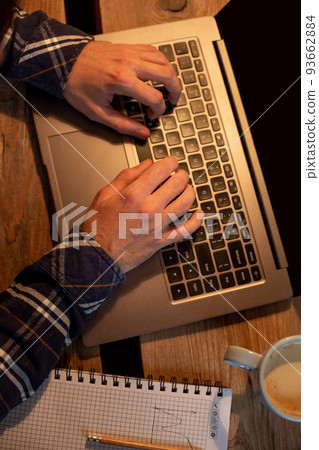 Young man drinking coffee in cafe and using laptop. Man's hands using laptop during coffee break Young man drinking coffee in cafe and using laptop. Man's hands using laptop during coffee break 93662884