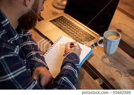 Cropped image of casual business man or freelancer planning his work on notebook, working on laptop computer with smart phone, cup of coffee on table at coffee shop or home office. Cropped image of casual business man or freelancer planning his work on notebook, working on laptop computer with smart phone, cup of coffee on table at coffee shop or home office. 93662886