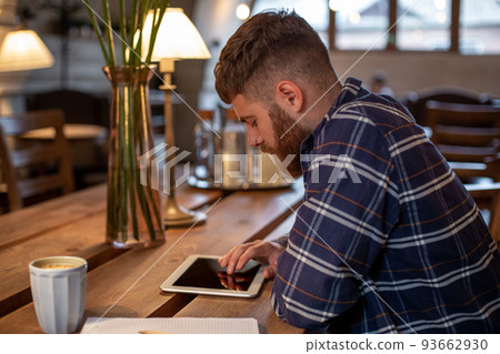 Freelancer dressed in casual outfit focus on reading news and looking on digital tablet while sitting in cozy urban cafe. Freelancer dressed in casual outfit focus on reading news and looking on digital tablet while sitting in cozy urban cafe. 93662930