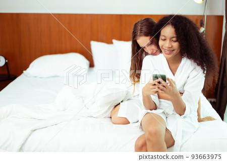 Caucasian and black women love together and hug hold as diversity person. Young Adult Romantic couple look at smart phone photo chat text as focus at blonde hair girl, copy space Caucasian and black women love together and hug hold as diversity person. Young Adult Romantic couple look at smart phone photo chat text as focus at blonde hair girl, copy space 93663975