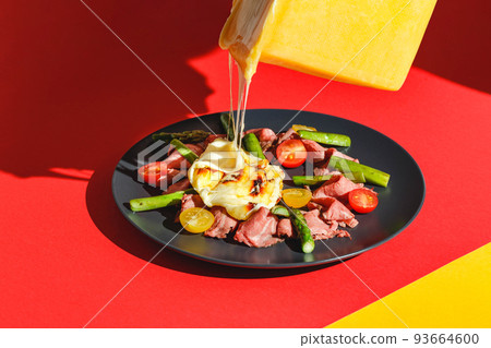 Delicious raclette cheese served over Roast Beef with Tomatoes and Asparagus, dish on red background. Hard light, deep shadow 93664600