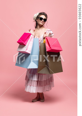 Shopping day. Vintage style portrait of pretty woman with long curly hair like girl of renaissance eras, lady-peasant isolated on pink background. Shopping day. Vintage style portrait of pretty woman with long curly hair like girl of renaissance eras, lady-peasant isolated on pink background. 93665622