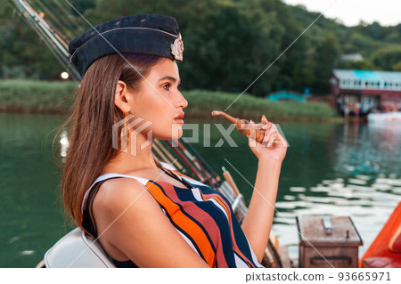 Summer. A woman in a cap with a pipe in her hands poses. Side view. Concept of sea trips 93665971
