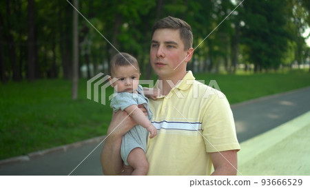 A young dad carries his son in his arms and kisses him. A man and his son are walking in the park against the backdrop of the forest. Big palm. A young dad carries his son in his arms and kisses him. A man and his son are walking in the park against the backdrop of the forest. Big palm. 93666529