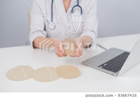 Woman plastic surgeon demonstrating breast implants at her desk.  93667416